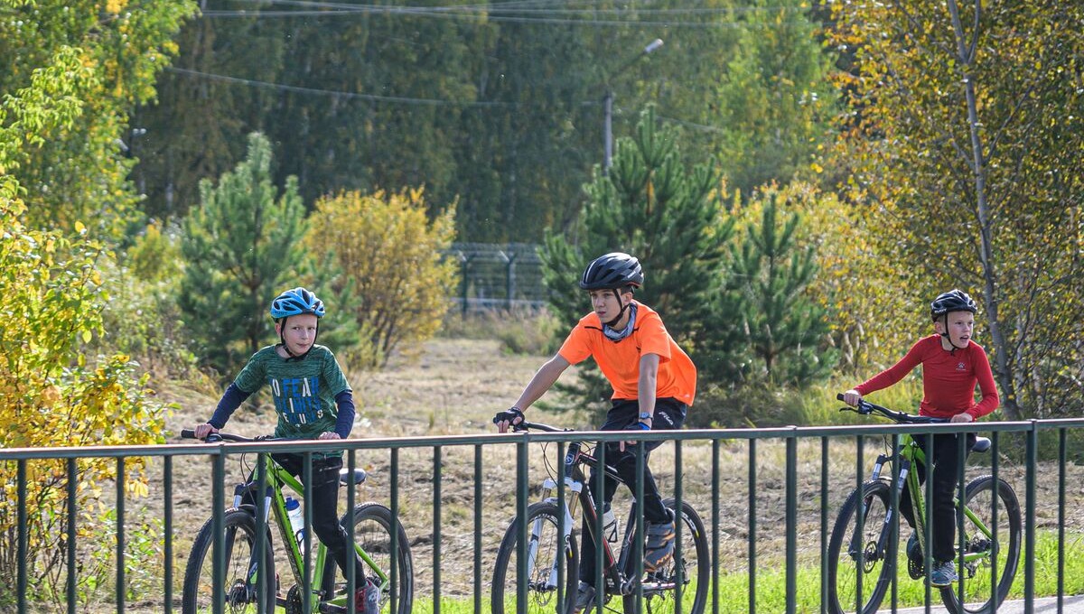 Three kids wearing helmets riding bikes along a path