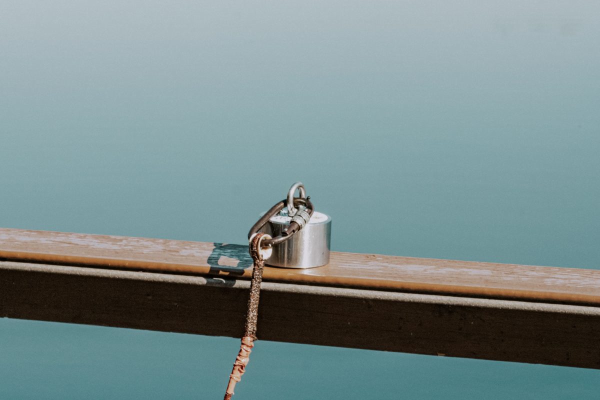 A fishing magnet and rope resting on a jetty railing above a calm lake