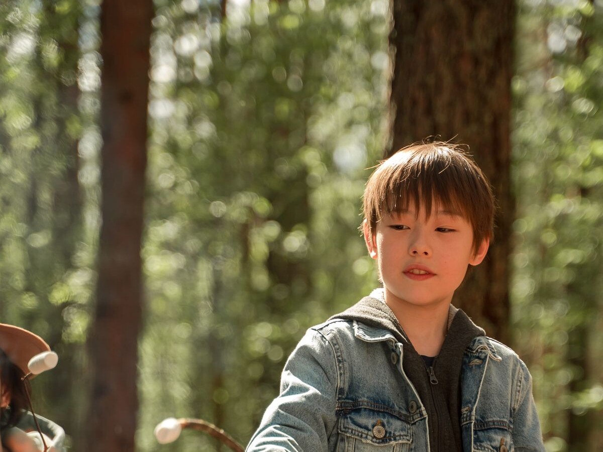 A boy roasting a marshmallow on a stick over a campfire in the forest